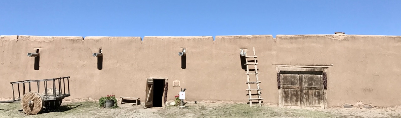 The front of an adobe hacienda, with ladder, rustic cart, and large wooden door