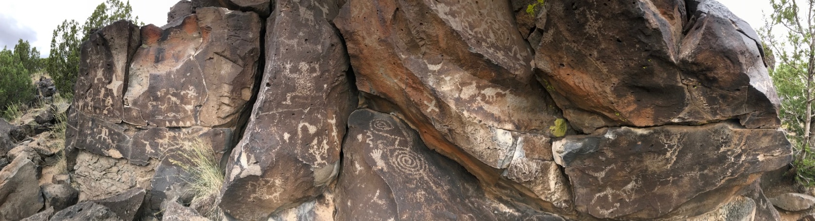 Panorama of tan petroglyphs carved into a brown rock