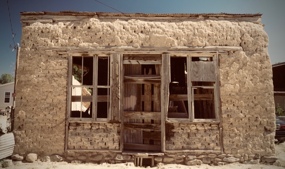 A broken-down mud brick house with no windowpanes and a rotting door