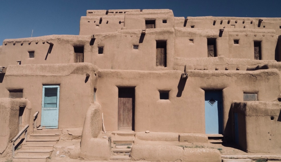 An adobe pueblo, three stories, with exterior doors on each level; doors on first level are light blue