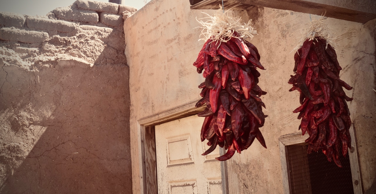 Two bundles of bright red dried chiles hanging in front of a mud brick house