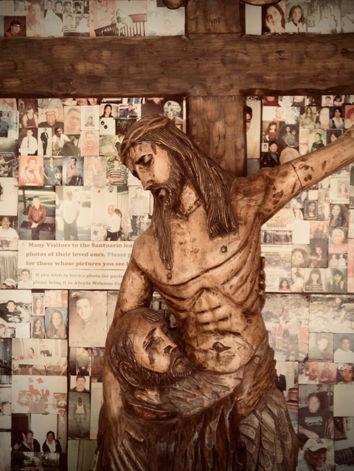 A figure of Christ on the Cross, held by Joseph of Arimathea, with photos of loved ones that others have prayed for behind him
