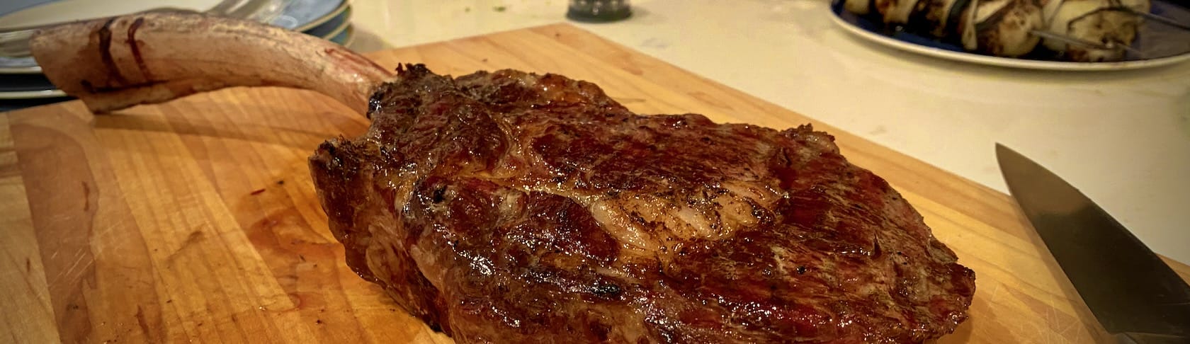 A well-crusted tomahawk steak, on a cutting board, next to a knife