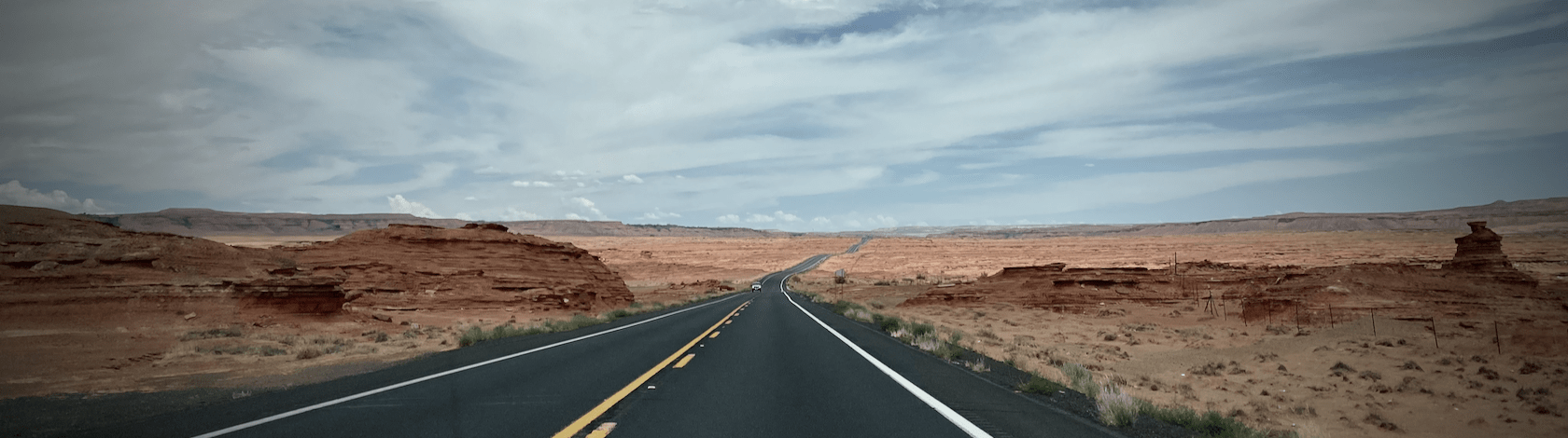 A highway heading into the desert distance, cutting through two sandstone hills and into feathery clouds