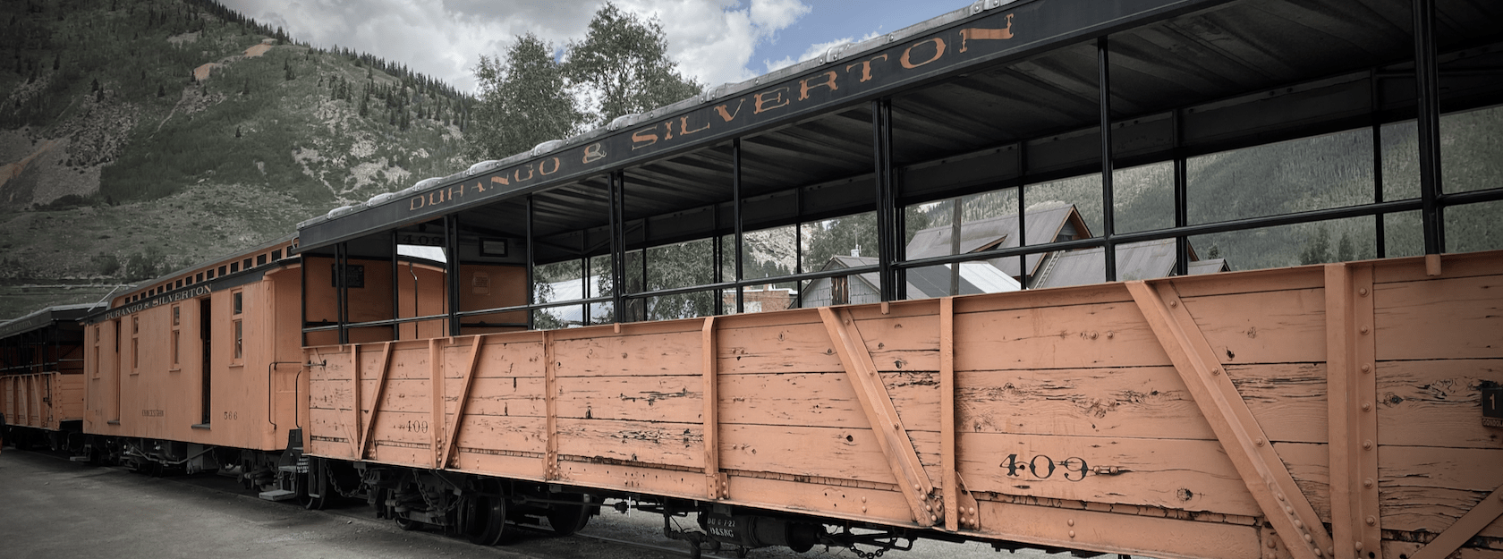 Weatherbeaten yellow railcars in front of a green Rocky mountain vista