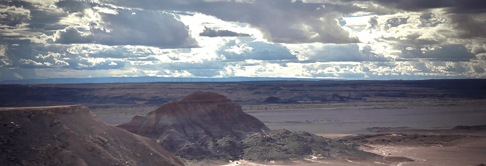 A desolate desert view with mountains of gravel and sand, below a cloudy sky